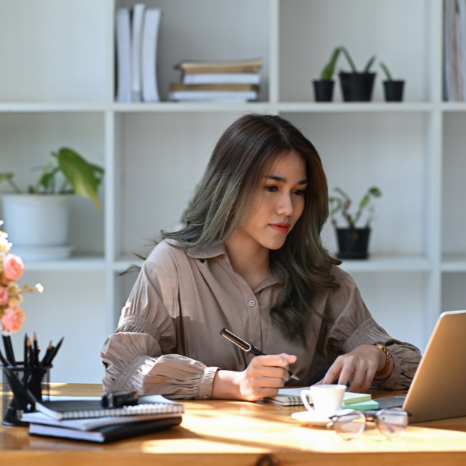 A woman reading a laptop screen, taking notes
